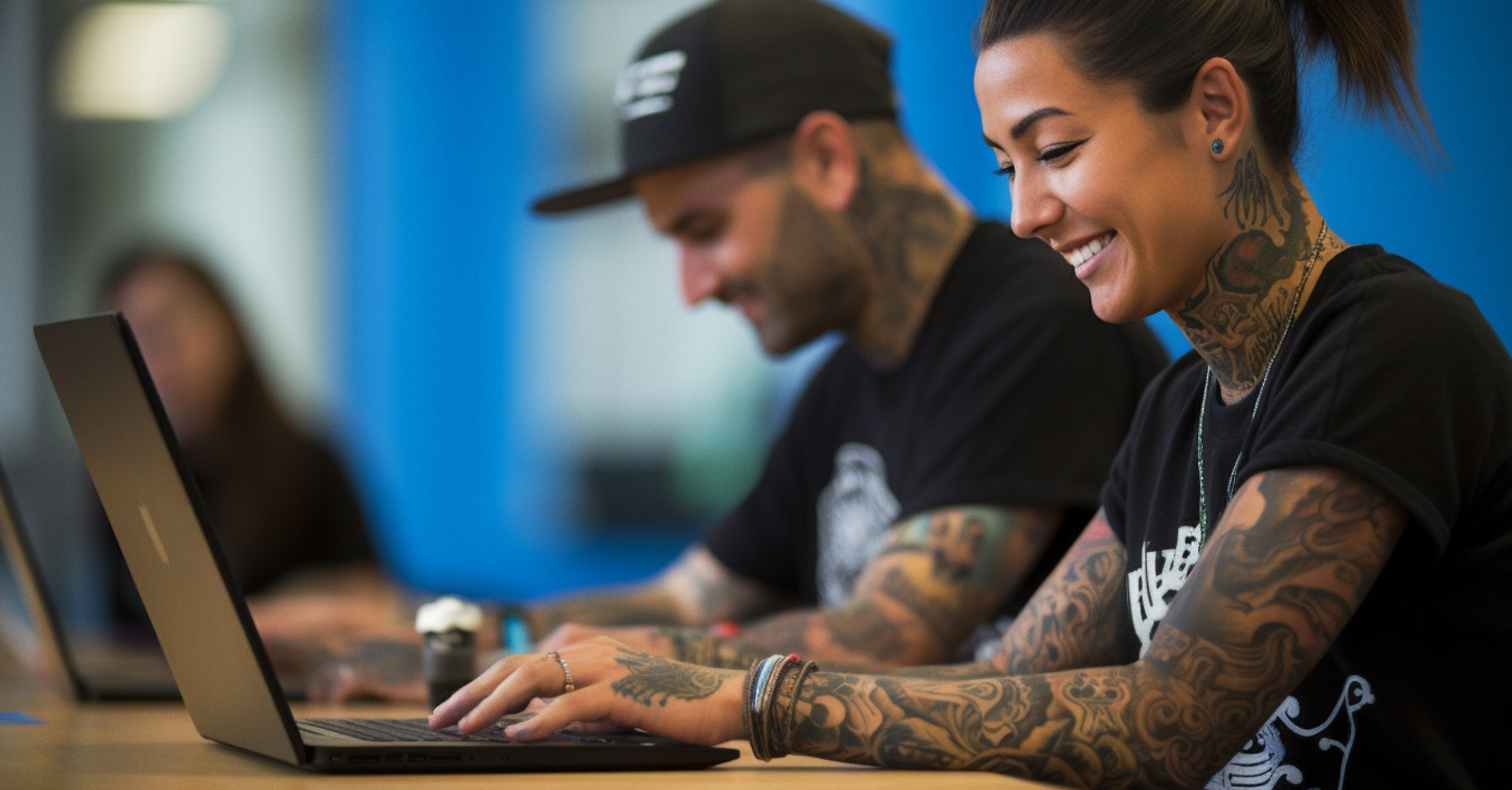 two tattooed Merch enthusiasts typing on computers placing Merch orders